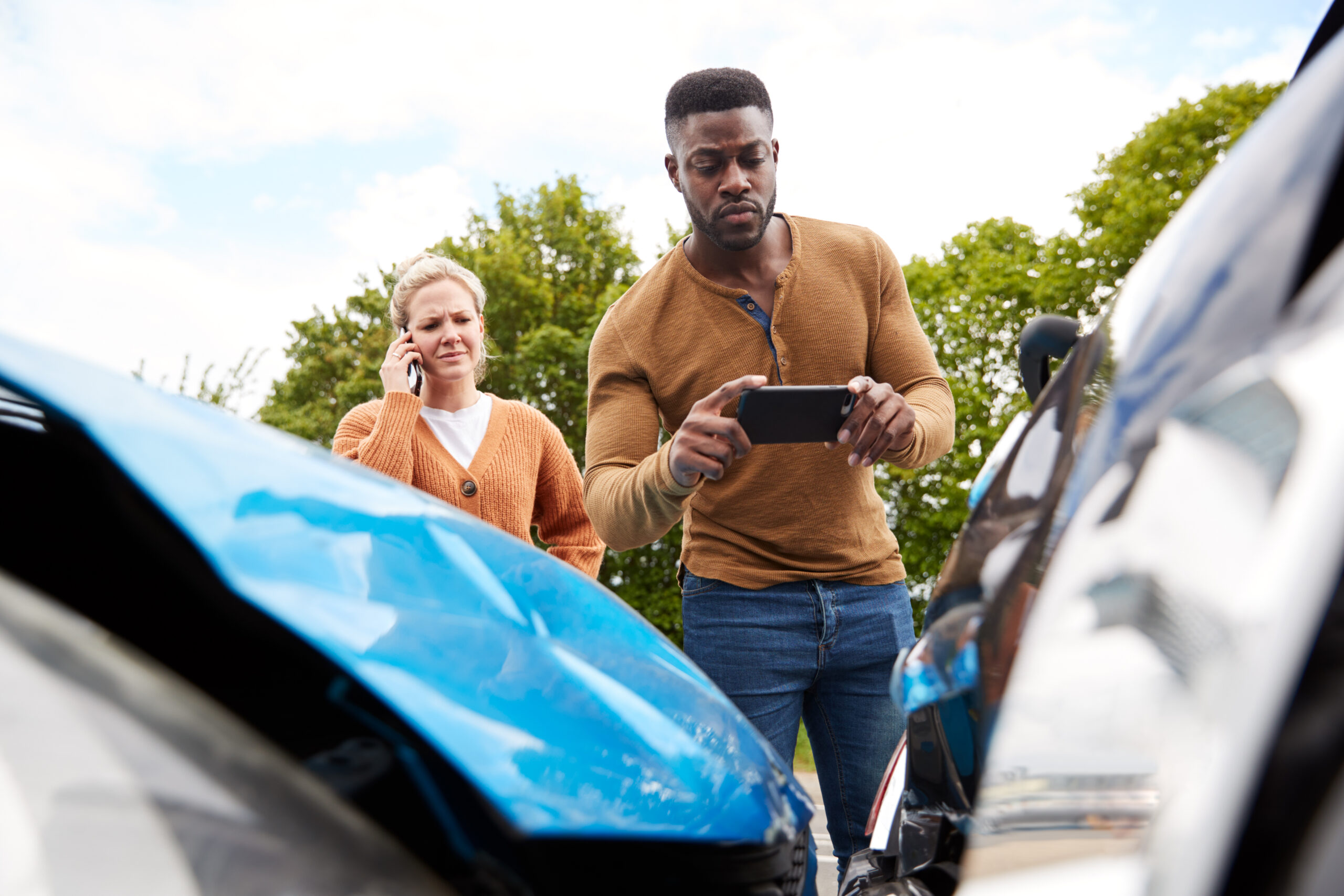 Man and woman taking pictures of vehicle damage after an accident.